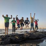 boy wearing green crew neck shirt jumping from black stone on seashore